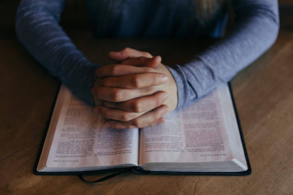 folded hands praying over the bible