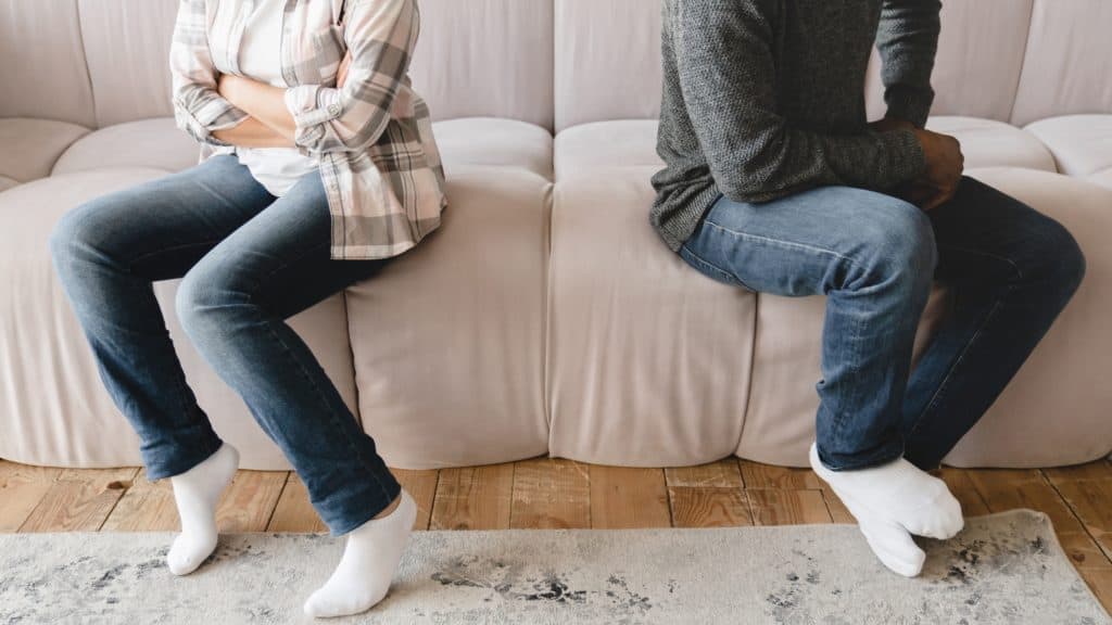 A couple sitting apart on a couch with their arms crossed and looking away from each other, representing a moment of disagreement. This scene can symbolize how healthy conflict in marriage requires space and time for both partners to reflect on their feelings.