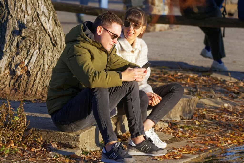 couple sitting by tree man on phone woman talking to him