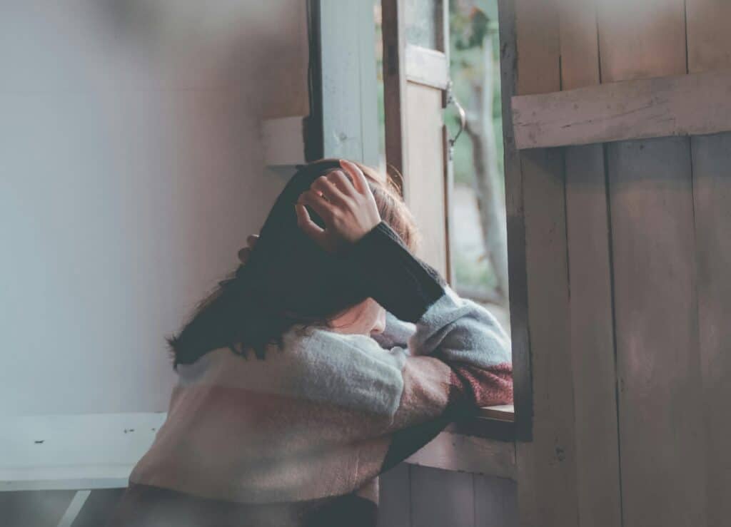 Young woman holding head sad in front of window