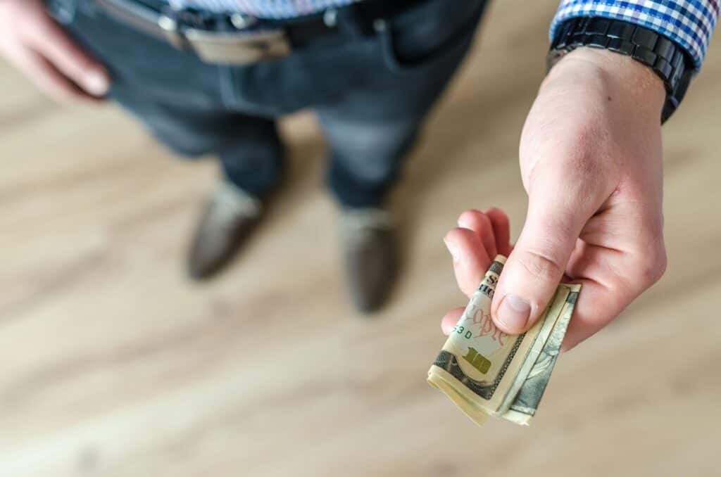 legs and hand of man holding ten dollar bills