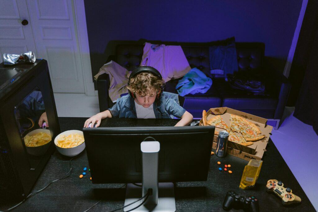 child surrounded by junk food pizza chips playing video games