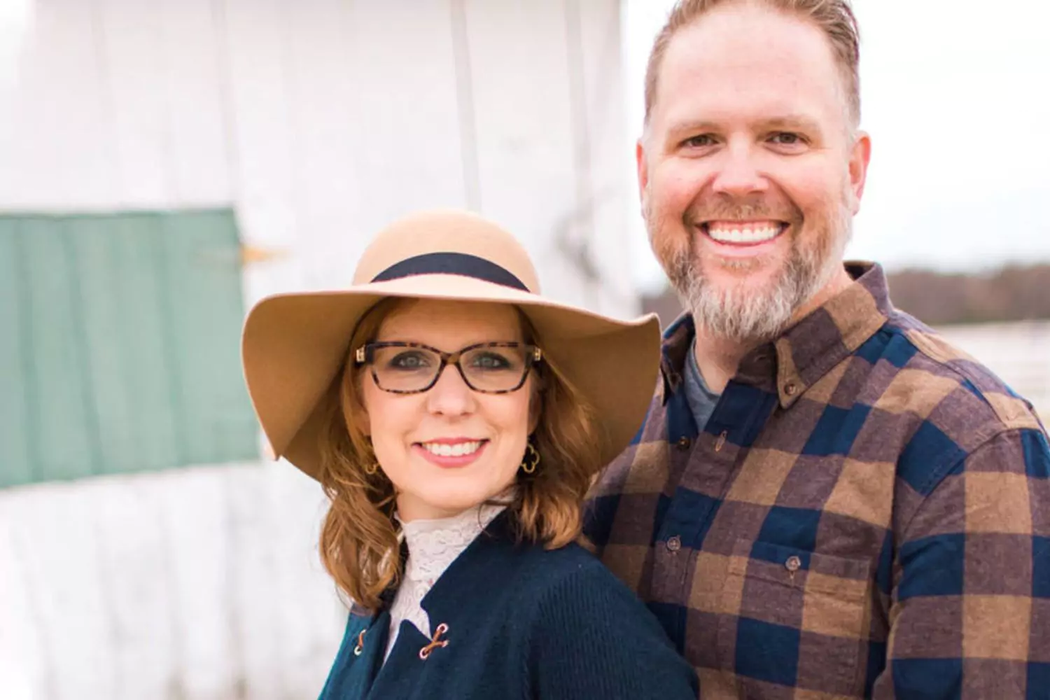 Bart Millard and his wife smile warmly in an outdoor setting, dressed in stylish yet cozy attire.