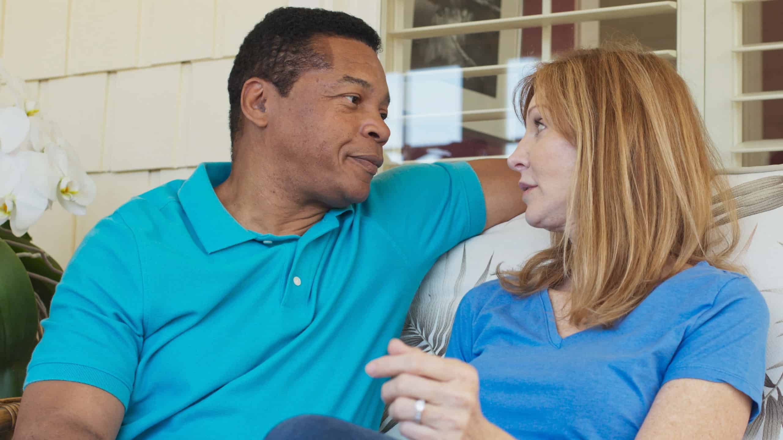 A husband and wife sit on their front porch and talk together