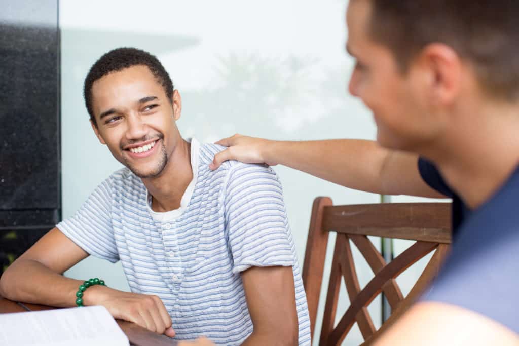 Two men sit at a table talking and encouraging one another, as one is a new father and the other is a Pregnancy Resource Center volunteer