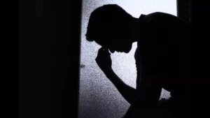 Shadow of a man with an abusive wife. He sits alone with his head in his hands, grappling with the fact that women abuse men too.
