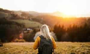 A rear view of senior woman walking outdoors in nature at sunset, hiking.