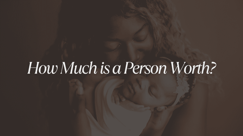 An image of a mother holding her child while the child sleeps with the larger caption in white that says: "How Much Is A Person Worth?"
